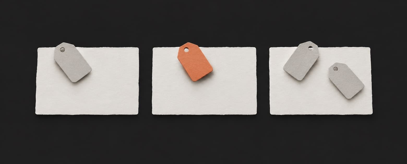 Three paper note cards on a dark table, each with small paper tags, one of the tags orange